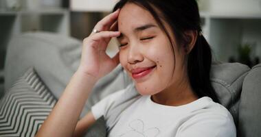 Handheld selective focus shot, Attractive young woman is sitting on a sofa, smiling happily while thinking about something in the living room at home. video