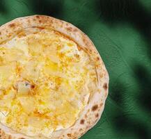 Pizza topped with cheese and pineapple on a green background photo
