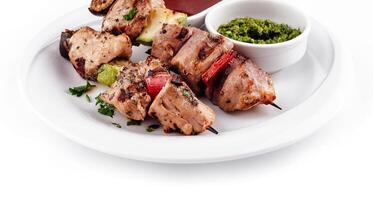 A la parrilla carne y vegetales en brochetas servido en blanco plato con salsas foto