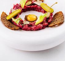 Deconstructed beef tartare with quail egg and rye bread close up photo