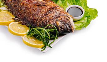 Grilled fish with lemon and greens served on a white plate photo
