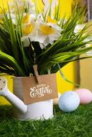 Vertical scene of daffodil flowers in watering can colorful eggs and card inscription Happy Easter photo