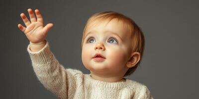 Baby with blue eyes reaching up excitedly while wearing a cozy sweater in a softly lit indoor setting photo
