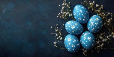 Colorful blue Easter eggs decorated with white flowers arranged on a dark background with delicate foliage photo