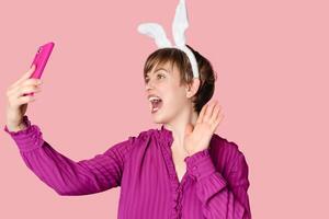 A beautiful girl with bunny ears on a colored background with a smartphone in her hands. photo