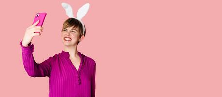 A beautiful girl with bunny ears on a colored background with a smartphone in her hands. photo