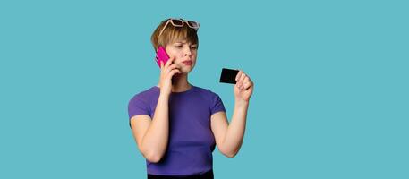 An incredulous pretty modern girl advertises, makes online purchases, holds a credit card in her hands and talks on a smartphone. Panoramic image photo