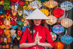 A woman in traditional Vietnamese clothes and a Non La hat on the background of lanterns in the ancient city of Hoi An. photo