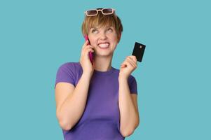An enthusiastic pretty modern girl advertises mobile banking, online shopping, holds a credit card in her hands and talks on a smartphone. photo