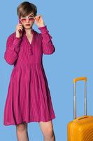 A young Caucasian woman using a smartphone and holding a suitcase, walking in front, is highlighted on a blue background photo