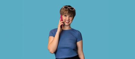 A Caucasian young woman is talking emotionally on a mobile phone on a blue background. Panoramic banner. A place for your text. Technology concept photo