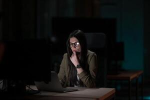 Female businesswoman employee working late in the office, using a laptop while feeling tired and burnt out. Reading, copywriting, editing, and struggling with fatigue and brain fog on a tight deadline photo