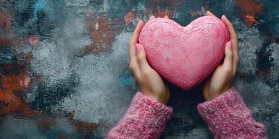 Hands holding a pink heart shaped stone against a textured background with soft colors in a cozy indoor setting photo