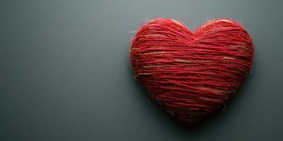 Textured red heart made of string resting on a simple grey background photo