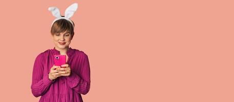A beautiful girl with bunny ears on a colored background with a smartphone in her hands. photo