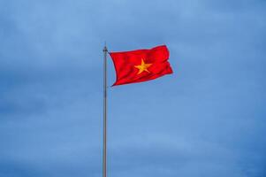 Vietnamese flag waving in the wind with clear blue sky. Yellow star on red background. photo
