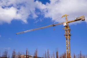 yellow tower crane on a background of blue sky with white clouds. Below is a grey concrete building under construction. photo
