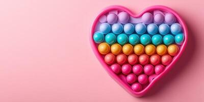 Colorful heart-shaped sensory toy filled with vibrant pop bubbles arranged in a playful pattern on pink background photo