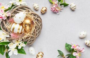 Easter eggs in a nest with spring flowers on a gray background photo