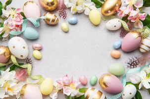 Easter eggs frame forming a circle on a gray background with flowers and feathers photo