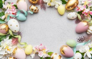 Easter eggs frame forming a frame on a gray background with flowers and feathers photo