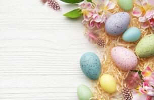 Easter eggs and spring flowers creating a frame on white wooden background photo
