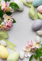 Easter eggs and spring flowers creating a frame on a concrete background photo