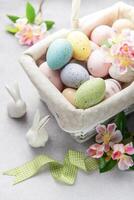 Pastel colored easter eggs in white wicker basket decorated with spring flowers photo