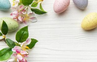 Easter eggs and flowers creating a frame on white wooden background photo