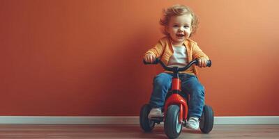 Child riding a tricycle indoors against an orange wall, enjoying playful moments photo
