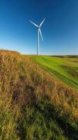 high tech wind turbine stands tall on green hill under clear blue sky photo