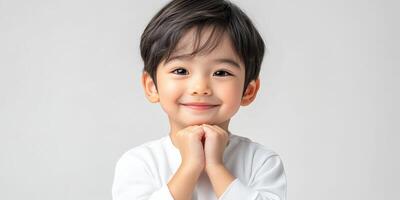 Young child smiles brightly with hands clasped, showcasing a joyful expression indoors in a neutral-toned environment photo