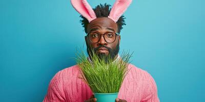 Man wearing bunny ears holds a pot of grass against a blue background during spring celebration photo