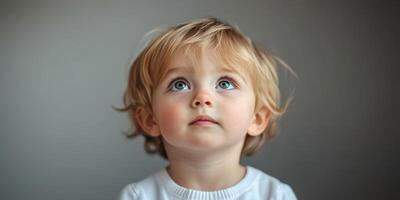 Child gazing up with curiosity while seated against a plain background in soft natural light photo