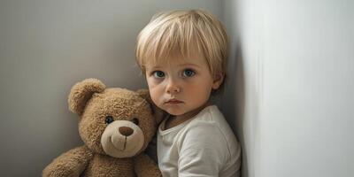 Child sitting in a corner with a teddy bear, showing a pensive expression in a cozy interior setting photo
