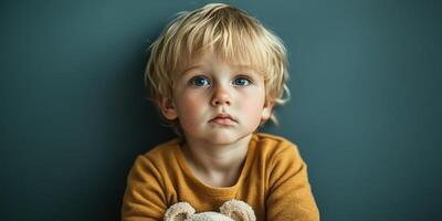 Young child with teddy bear gazes thoughtfully against a simple backdrop indoors photo