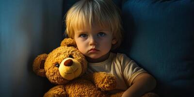 Sad child holding teddy bear in dimly lit room with soft shadows during evening photo