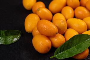 Vibrant kumquats, adorned with water droplets, create a captivating display alongside glossy green leaves on a dark background photo