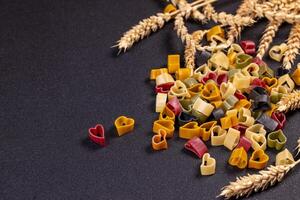 Small colorful heart shaped pasta is arranged on a black background with wheat, creating a romantic and culinary scene photo