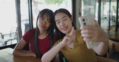 Handheld shot, Two Asian women are enjoying taking selfies together on mobile phone at a table in a coffee shop. Family enjoying time together. Happy lifestyle. video