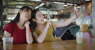 Handheld shot,Two Asian women are enjoying taking selfies together on mobile phone at a table in a coffee shop. Family enjoying time together. Happy lifestyle. video