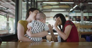Two Asian young women are playing with a little boy, sharing a warm moment together in a coffee shop atmosphere. Family enjoying time together. Happy lifestyle. video