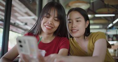 Two siblings are talking and enjoying watching a funny clip on smartphone while sitting at a table in a coffee shop. Happy lifestyle. video