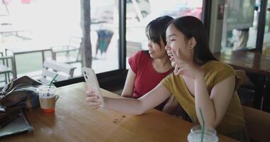 Two Asian women are enjoying taking selfies together on mobile phone at a table in a coffee shop. Family enjoying time together. Happy lifestyle. video