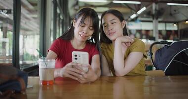 Handheld selective focus shot,Two siblings are talking and enjoying watching a funny clip on smartphone while sitting at a table in a coffee shop. video
