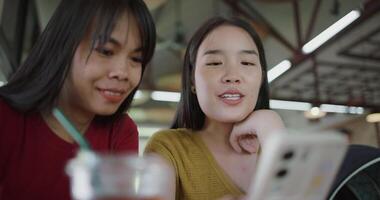 Handheld selective focus shot, Two siblings are talking and enjoying watching a funny clip on smartphone while sitting at a table in a coffee shop. Happy lifestyle. video