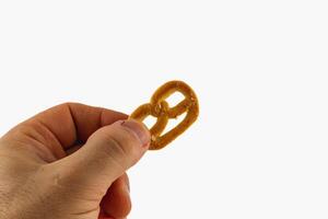 Hand holding a small pretzel against a bright background in a kitchen photo