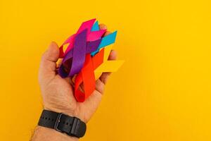 Multiple colorful awareness ribbons held in a hand against a bright background photo