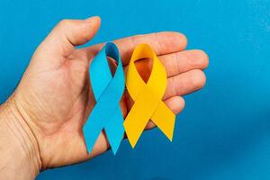 Hand holding blue and yellow awareness ribbons for health campaigns photo
