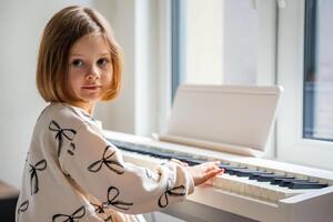 Home lesson on music for the girl on white piano synthesizer. Concept of early development. learning music enhances motor skills, hearing, and intelligence, fostering creativity from childhood. photo